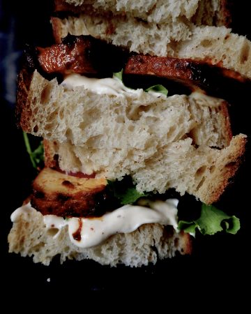 de sandwich van dichtbij, brood, tofu, aioli, en sla gestapeld tegen een donkere achtergron