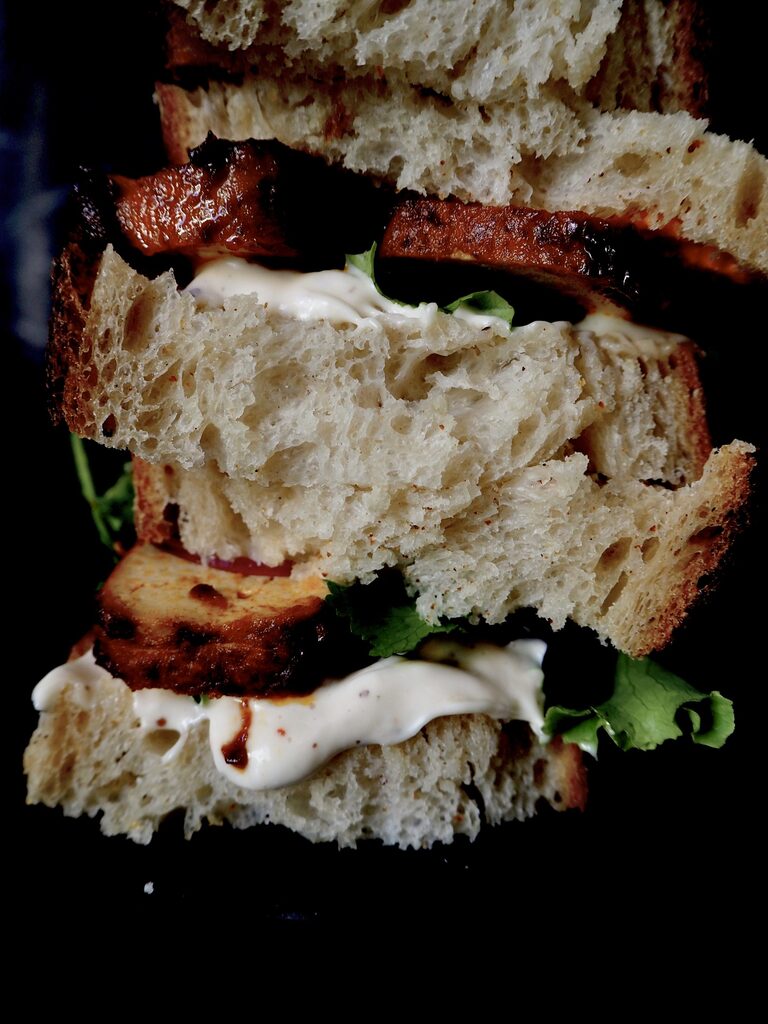 de sandwich van dichtbij, brood, tofu, aioli, en sla gestapeld tegen een donkere achtergron