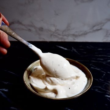 easy vegan aioli seen from front view in a small bowl with a silver spoon and a hand against a dark and light backdrop