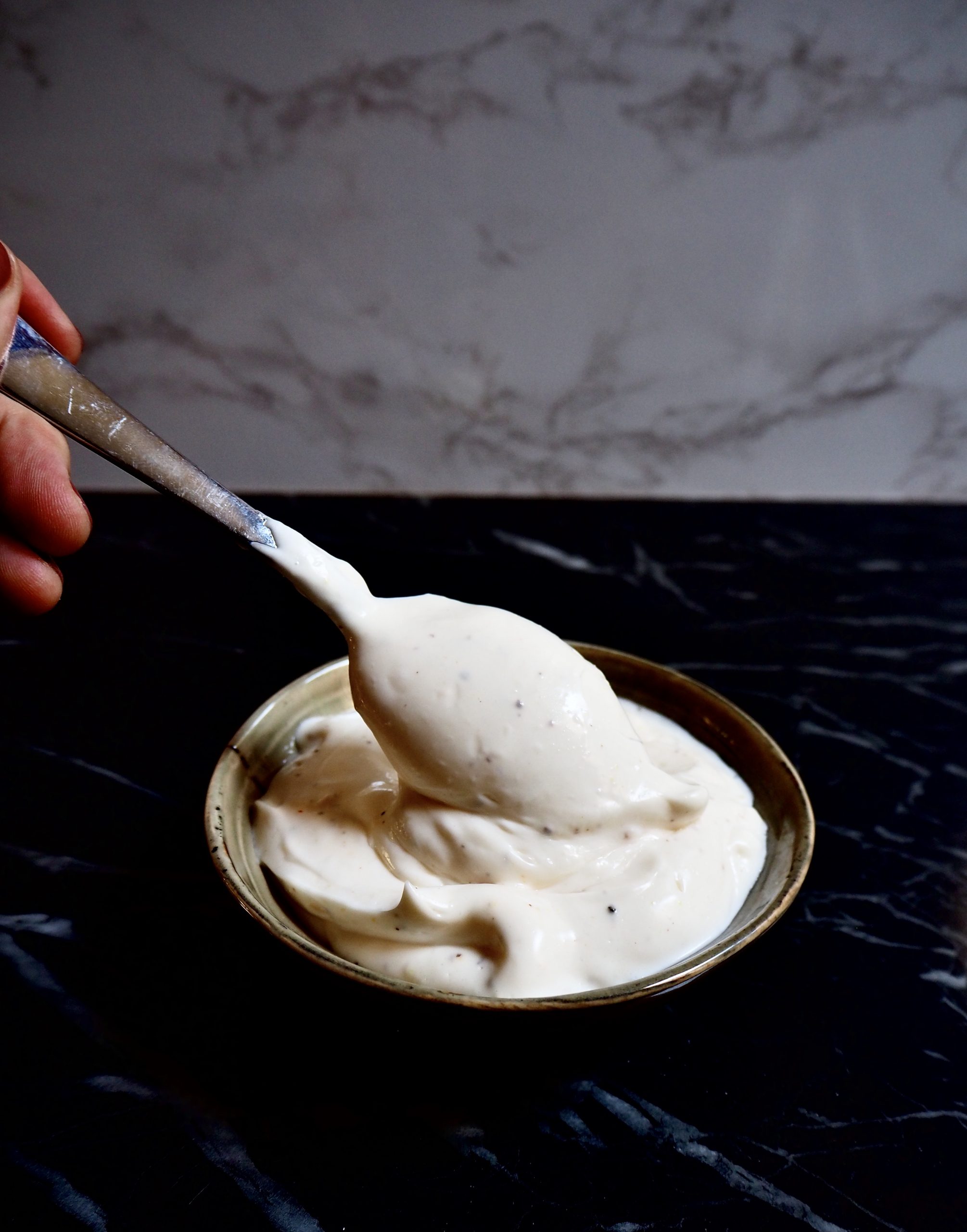 easy vegan aioli seen from front view in a small bowl with a silver spoon and a hand against a dark and light backdrop