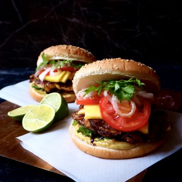 two onion bhaji burgers and a chopped up lime against a dark background