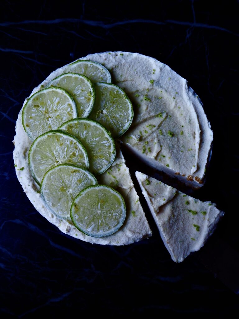 no bake lime cheesecake seen from above with a slice cut from the lower side against a dark backdrop