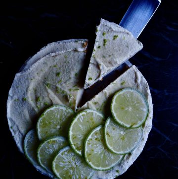 no bake limoen cheesecake vanaf bovenaf gezien met een stukje dat geserveerd wordt in de rechter bovenhoek. tegen een donkere achtergrond