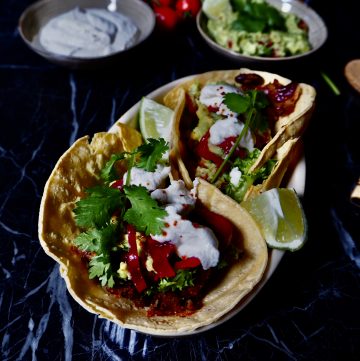 15 minute vegan tacos in a bowl seen from the front with two small bowls in the background with sour cream and guacamole. Against a dark backdrop