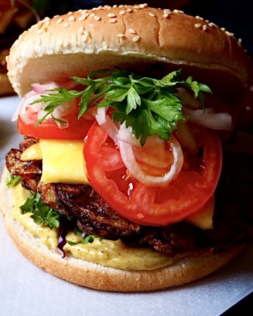een bhaji burger van dichtbij gezien. een broodje met curry mayo, sla, bhaji, mango, tomaat, ui, koriander.