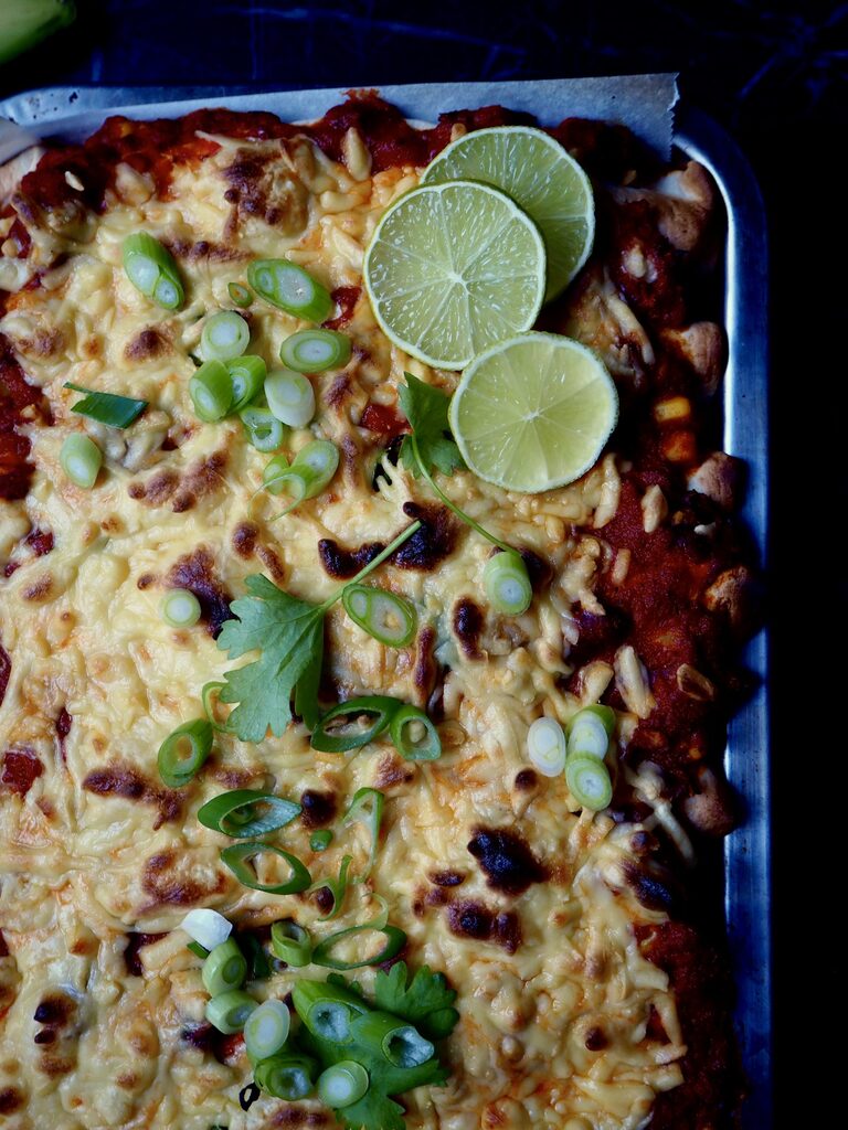 enchiladas with roasted vegetables seen from above topped with coriander, spring onion and lime.