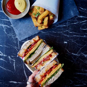 la polenta crujiente estilo patatas fritas y los sandwiches con filete de polenta vistos desde arriba con una mano izquierdo tomando uno de los sandwiches
