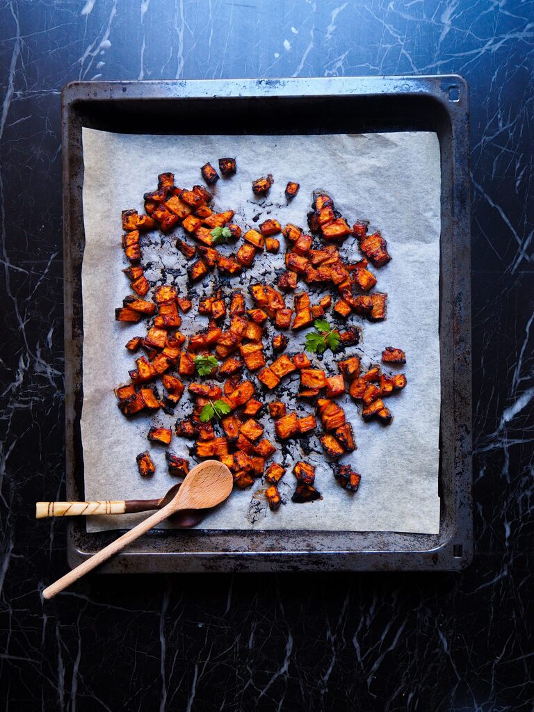miso glazed sweet potato cubes just from the oven seen from above on a baking sheet with parchment paper and two spoons