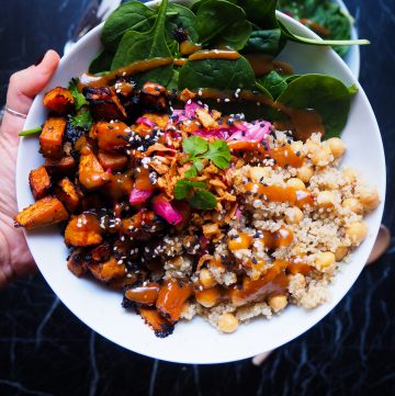 bowl with miso glazed sweet potato, quinoa, spinach, chickpeas, miso vinaigrette, red onion, and crispy onion on top seen from up close