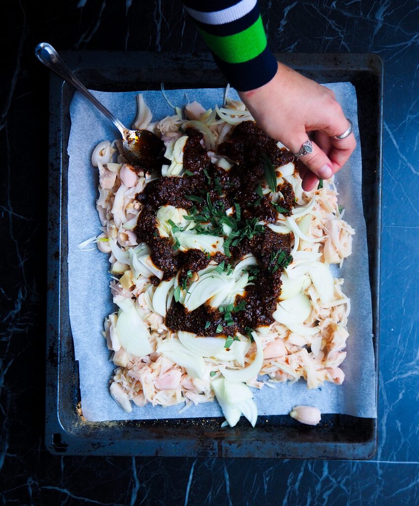 de jackfruit op een ovenschaal met ui en knoflook en de bbq saus met een linkerhand die verse salie strooit