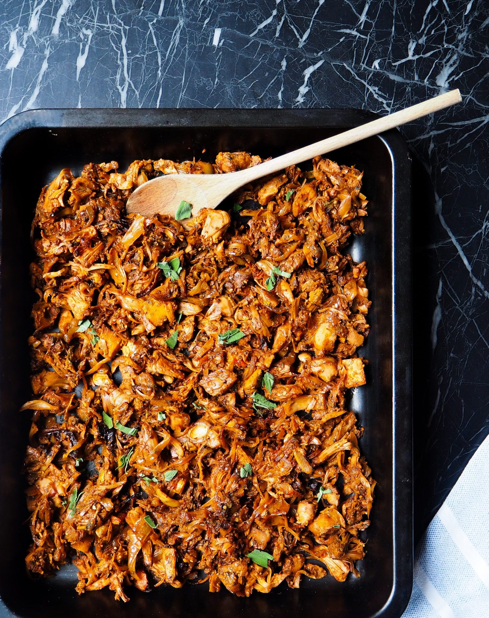 jackfruit bbq-salvia en la bandeja de horno con una cuchara de madera y trozos de alvia visto de arriba