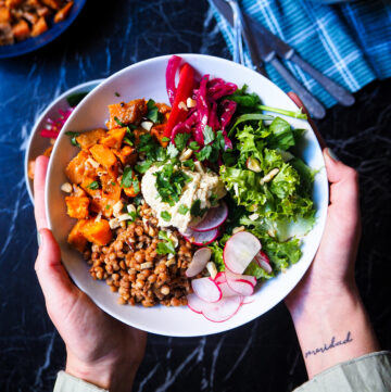 a spiced lentil and sweet potato bowl held by two hands seen up close