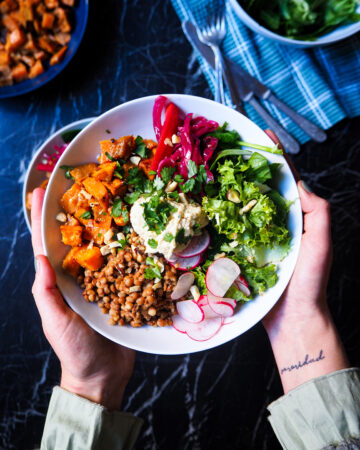 a spiced lentil and sweet potato bowl held by two hands seen up close
