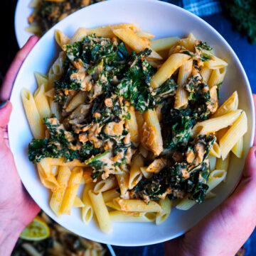 a bowl of cheesy hummus pasta held by two hands seen up close