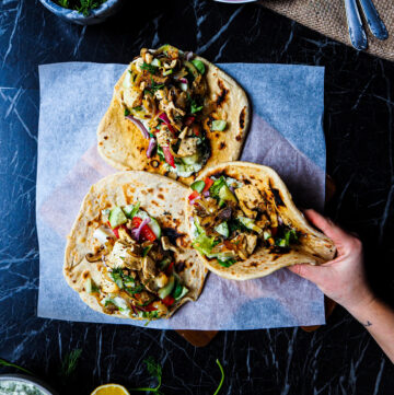 three vegan tofu and shiitake gyros seen from above with a hand grabbing one.