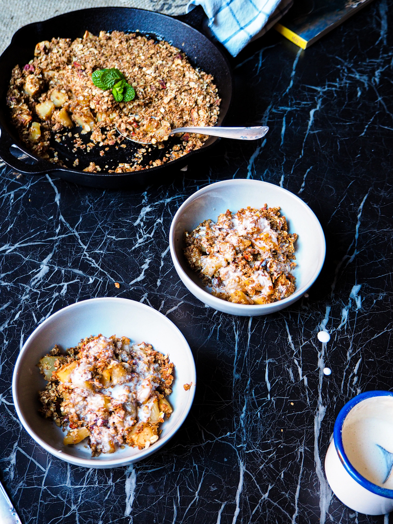 a skillet with vegan apple crumble and two bowls seen from a front view against a dark backdrop