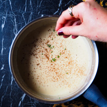 salsa béchamel vegana vista de arriba con una mano echando tomillo fresco