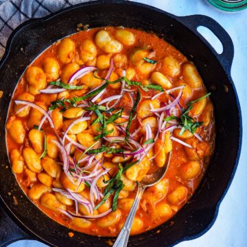 cast iron skillet seen from top down with spicy curried butter beans against white tablecloth backdrop