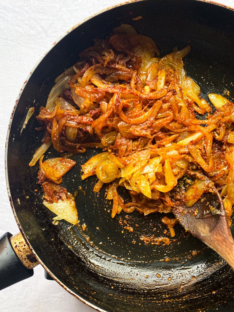 caramelising onions with spices in pan with wooden spoon